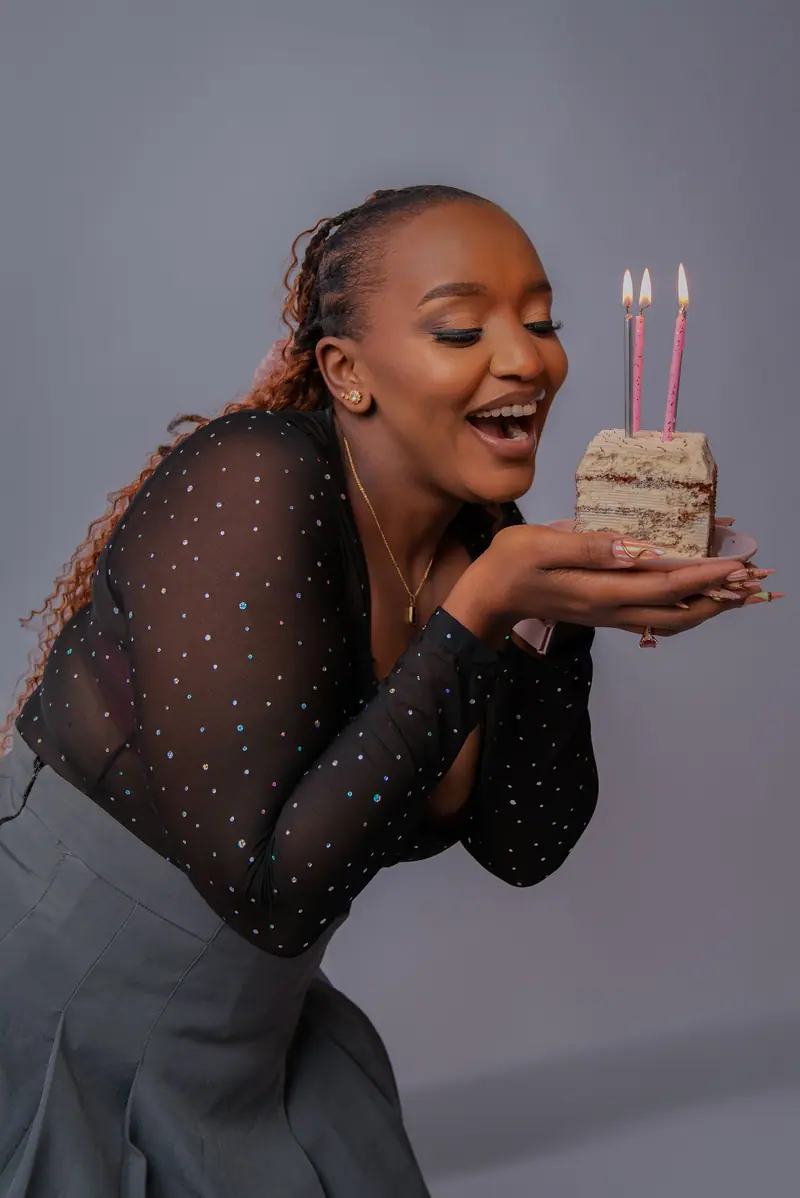 Woman in a sheer sparkle top leaning in to blow out birthday candles on a slice of cake